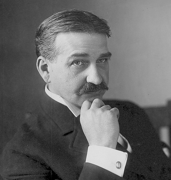 Photo of L. Frank Baum sitting in a suit with a mustache and his chin resting on one fist and his cufflink showing.