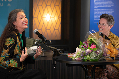 Ana Castillo and Christine Rice sitting at a table in from of microphones while Christine interviews Ana after Ana received the Fuller Award in 2022.